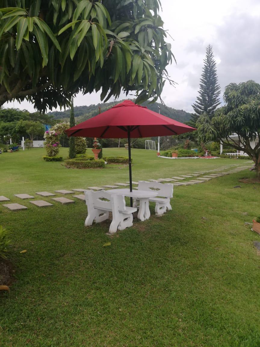 Mesa blanca con sombrilla roja bajo un árbol en el jardín